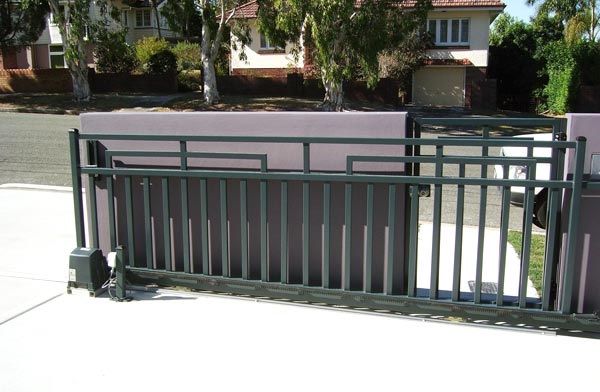 Dark green aluminium sliding gate on its track beside a rendered wall