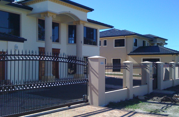 Black aluminium infill panels and sliding gate between rendered piers in front of a two-storey home