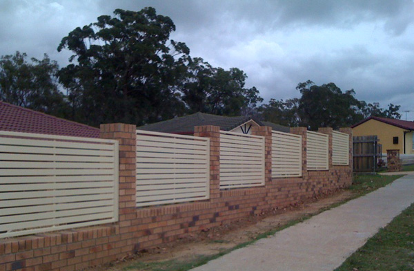 Cream aluminium slat panels set between red brick piers along a footpath